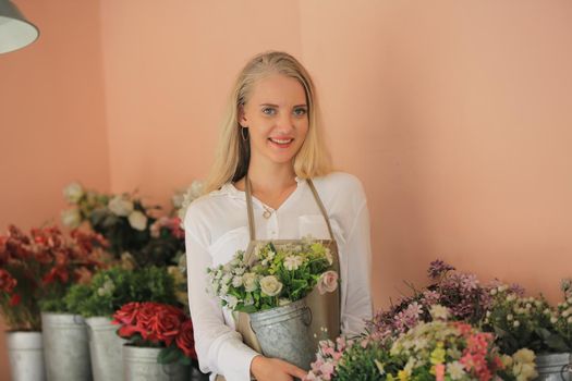 Beautiful blonde hair girl standing with confidence in front of flower in open retails flora shop. Small business owner concept.