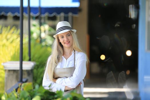 Beautiful blonde hair girl standing with confidence in front of flower in open retails flora shop. Small business owner concept.