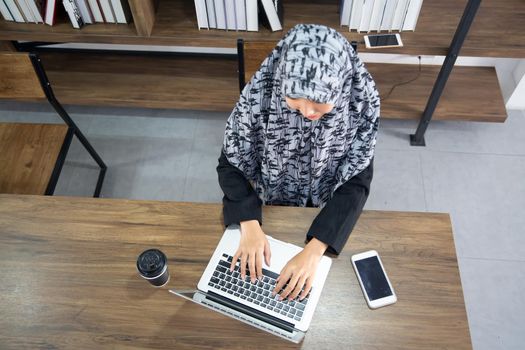 young Muslim woman using a laptop in a modern office