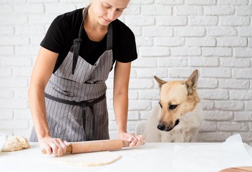 Home cooking. Woman kneading dough at home with her dog sitting by