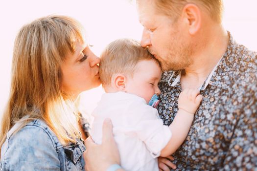 Happy family - mom and dad are holding a little son in their arms and kissing by the sea near the water, close-up. High quality photo