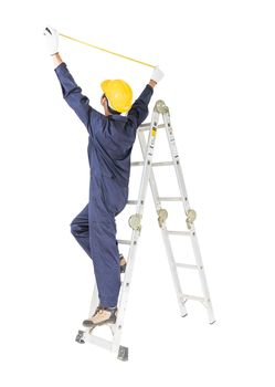 Young handyman in uniform standing on ladder while using tape measure on white, Cutout isolated on white background