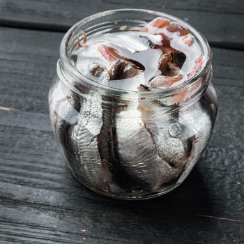 Pickled Anchovy set, in glass jar, on black wooden table background, square format