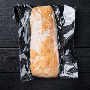 Ciabatta in a plastic bag, on black wooden table background, top view flat lay