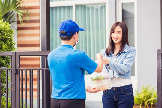 Asian young delivery man wear face mask he making grocery service giving rice food boxes plastic bags to woman customer receiving door at house after pandemic coronavirus, Back to new normal concept