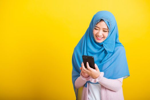 Asian Muslim Arab, Portrait of happy beautiful young woman Islam religious wear veil hijab funny smile she using hold mobile smart phone reading social media isolated on yellow background