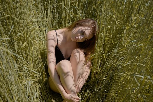beautiful young woman sitting in the grass on the spring green field