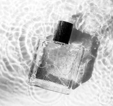 Perfume and drops in black and white. Perfume bottle and flowers on the background and water drops. A bottle of perfume without inscriptions . Smell. Water drops. Copy space. Article about the choice of perfume