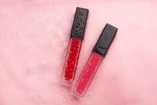 Lip gloss and water drops on a pink background. The concept of a bottle of lip gloss without labels. Cosmetology. Decorative cosmetics. Copy space