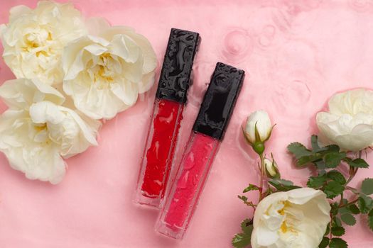 Lip gloss with flowers and water drops on a pink background. The concept of a bottle of lip gloss without labels. Cosmetology. Decorative cosmetics. Copy space
