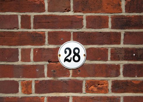 Number 28 on old red brick wall. Black number 28 on white round house plate. Antique UK house number