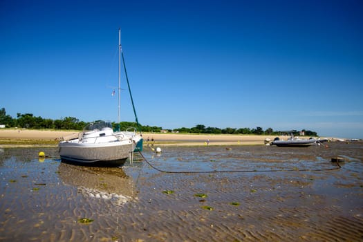 a sailing boat and a motorboat laying on the beach of plage de la Loge at Portes-en-Ré at lowtide on a sunny summertime on the Isle of île de re in the Charente-Maritime in France