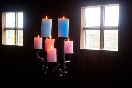 Standaard with colored candles in wooden cabin with daylight shinning through the windows
