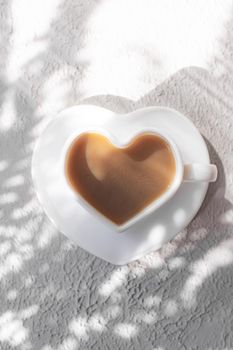 A cup of cappuccino on a saucer and shade from the sun. Coffee drink. Copy space. A heart-shaped cup. Relax
