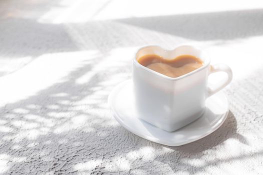 A cup of cappuccino on a saucer and shade from the sun. Coffee drink. Copy space. A heart-shaped cup. Relax