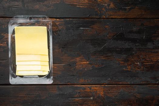 Yellow cheese slices of cheddar set, in plastic pack, on old dark wooden table background, top view flat lay, with copy space for text