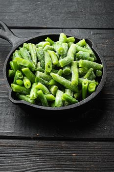 Green beans. Fresh frozen beans for salad, cooking or raw vegan food set, in frying cast iron pan, on black wooden table background
