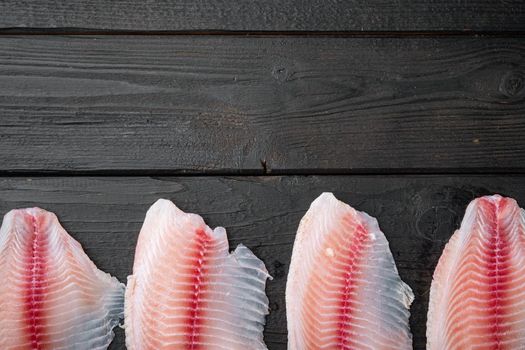 White tilapia fish fillet cuts on black wooden table, top view with copy space for text