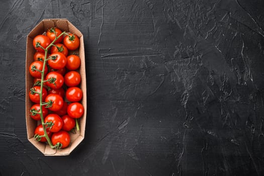 Cherry tomatoes on branch set, in container, on black stone background, top view flat lay, with copy space for text