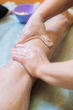 The spa master applies a scrub to the leg of a young girl. Close-up.
