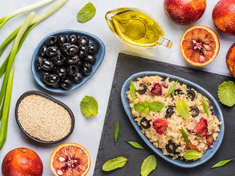 Salad with quinoa, red orange, black olives, green onion, mint and olive oil on gray concrete backkground. Vegan food. Top view or flat lay.