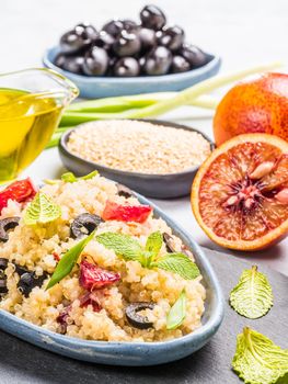 Salad with quinoa, red orange, black olives, green onion, mint and olive oil on gray concrete backkground. Vegan food. Vertical.