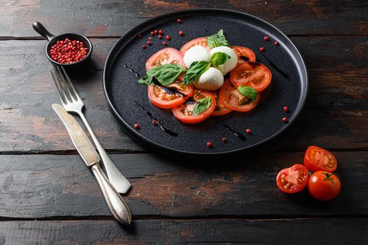 Caprese salad Tomato and mozzarella slices with basil leaves on olive wood dark table .