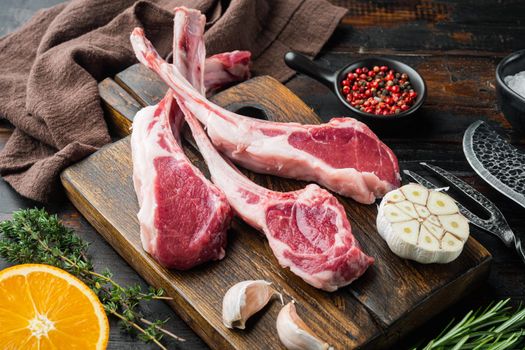 Fresh chopped calf Racks of lamb ready for cooking set, with ingredients carrot orange, herbs, on old dark wooden table background