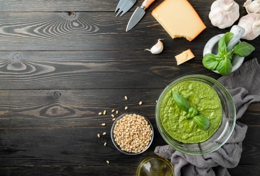 Italien cuisine. Preparing homemade italian pesto sauce. Fresh pesto in bowl with ingredients, top view flat lay on black wooden table, copy space