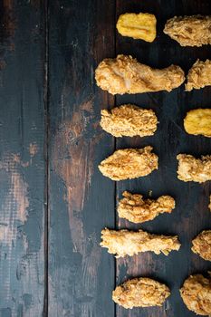 Breaded fried chicken parts on dark wooden background, flat lay, with space for text.