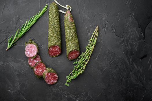 Fuet salami sausage in herbs on black background, top view with copy space.