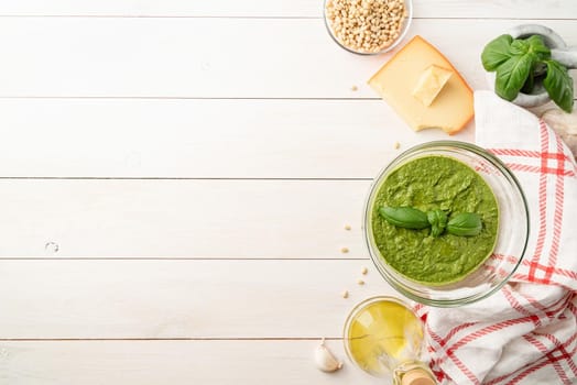 Italien cuisine. Preparing homemade italian pesto sauce. Fresh pesto in bowl with ingredients, top view flat lay on white wooden table, copy space