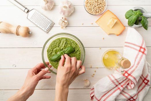 Italien cuisine. Preparing homemade italian pesto sauce. Fresh pesto in bowl with ingredients, top view flat lay on white wooden table, copy space