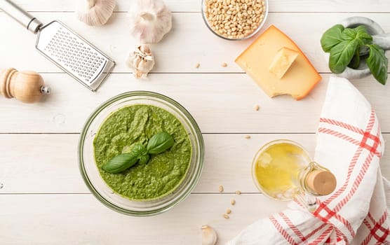 Italien cuisine. Preparing homemade italian pesto sauce. Fresh pesto in bowl with ingredients, top view flat lay on white wooden table