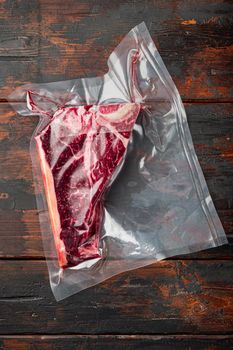 Raw meat T bone steak in vacuum plastic bag for sous vide cooking set, on old dark wooden table background, top view flat lay