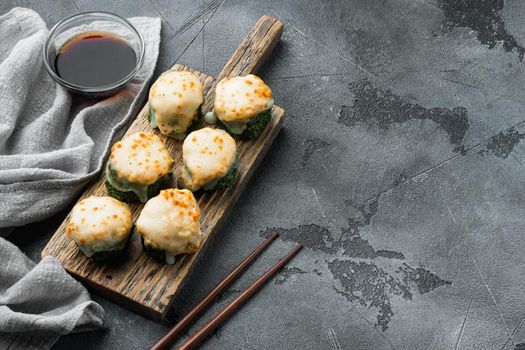 Baked sushi maki rolls with salmon, crab, cucumber, avocado, flying fish roe and spicy sauce set, on gray stone background , with copyspace and space for text