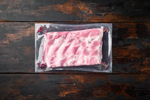 Vacuum packaging with raw pork rib set, on old dark wooden table background, top view flat lay, with copy space for text