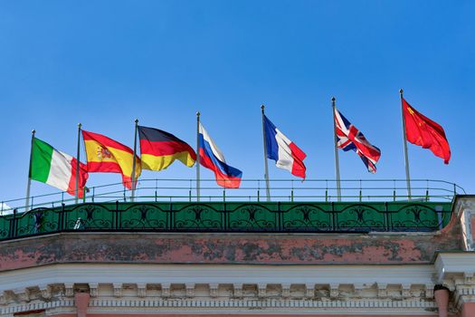 Flags of different countries on the roof of a building in the wind against a background of blue sky