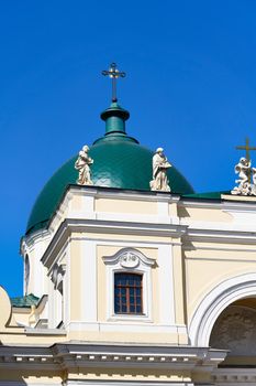 Green dome with a cross and a roof with sculptures against the blue sky. Fragment of the christian church