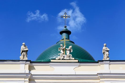 Green dome with a cross and a roof with sculptures against the blue sky. Fragment of the christian church