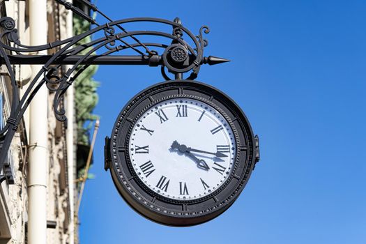 Antique round clock with Roman numerals hang on the street of the city. Close up