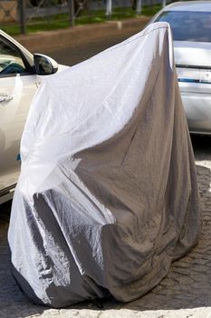 Bike covered with tarpaulin is parked on the street on a hot sunny summer day. Close up