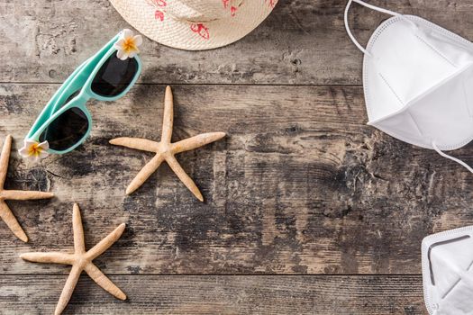 Sunglasses, starfish, summer hat and protective face mask on wooden background. Coronavirus summer concept.