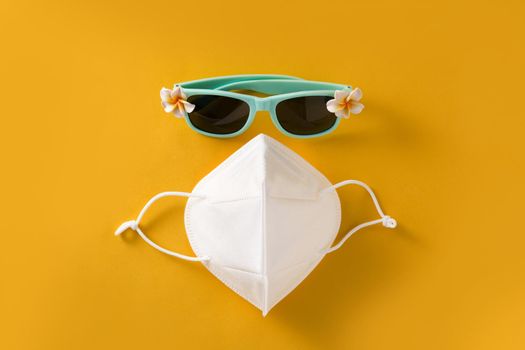 Sunglasses and protective face mask on yellow background. COVID-19 summer concept.