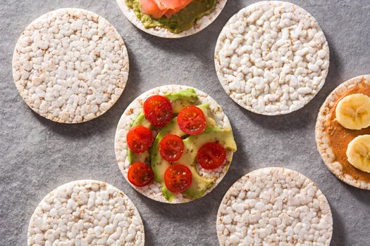 Puffed rice cakes with guacamole salmon,tomato and avocado, and banana with peanut butter on gray stone background