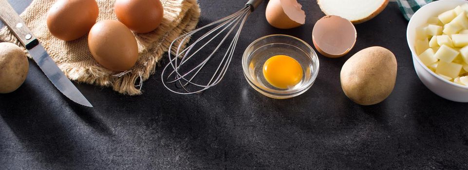 Spanish omelette tortilla ingredients: eggs, potatoes and onion on black slate background. Top view copy space