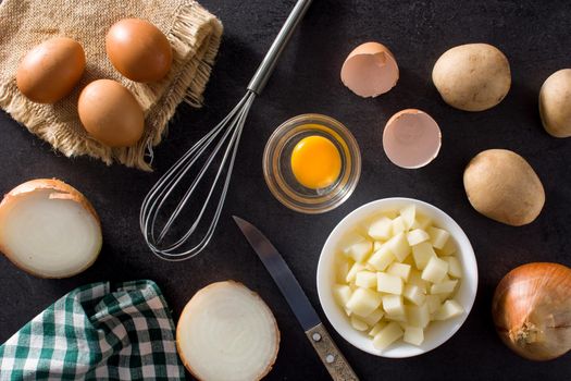 Spanish omelette tortilla ingredients: eggs, potatoes and onion on black slate background