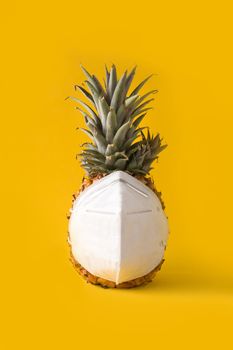 Pineapple with protective face mask on yellow background. Summer COVID-19 concept