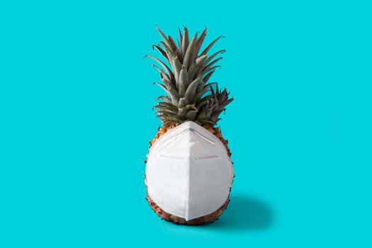 Pineapple with protective face mask on blue background