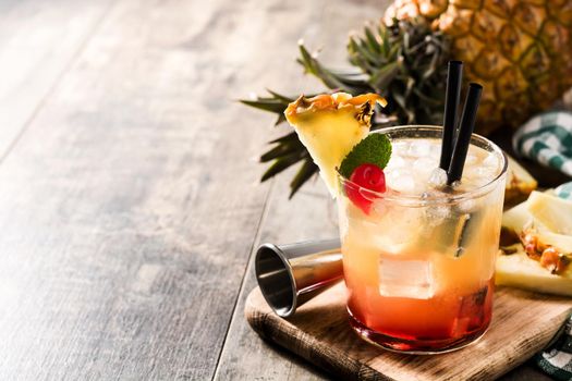 Cold mai tai cocktail with pineapple and cherry on wooden table